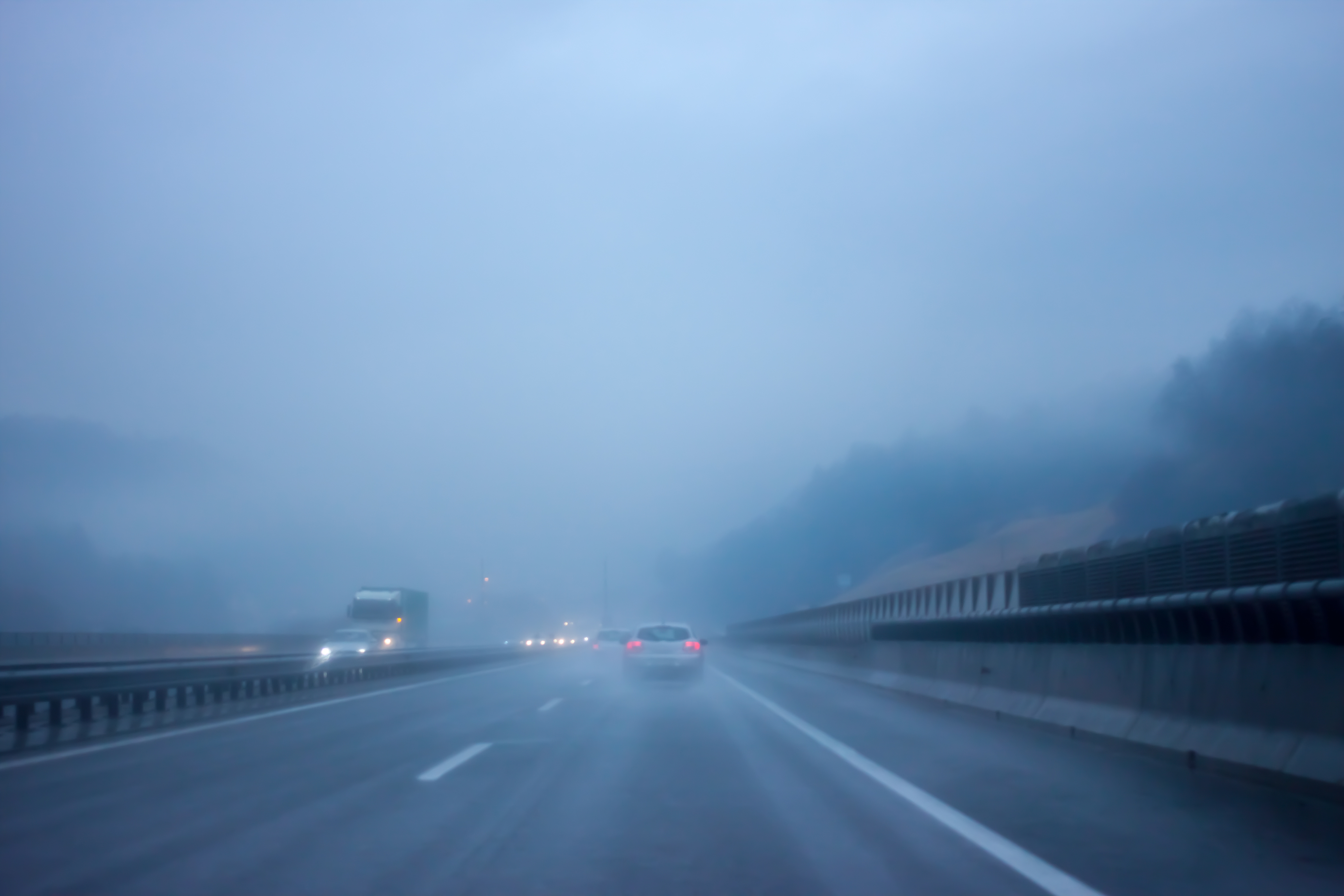 Ein Auto fährt bei starkem Regen auf einer nassen Straße und verdeutlicht die Herausforderungen bei widrigen Wetterbedingungen