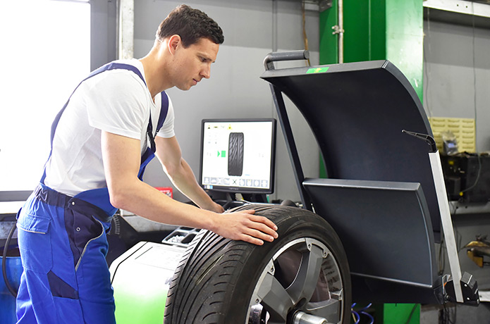 Autoreifen wird in einer Kfz-Werkstatt auf einer Auswuchtmaschine ausgewuchtet.