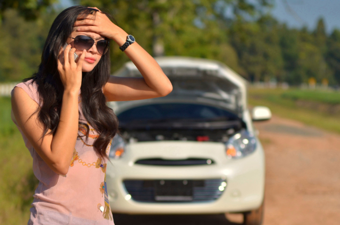 Eine Frau telefoniert mit verzweifeltem Blick. Hinter ihr ein Auto mit Motorüberhitzung.